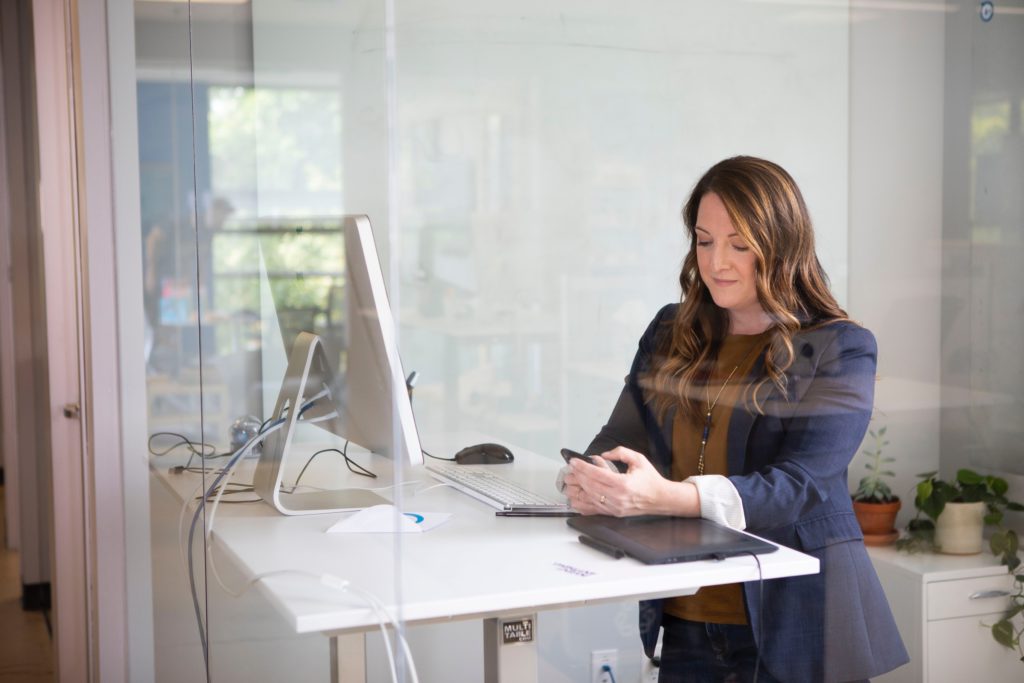 Woman checking her phone standing at desk with laptop